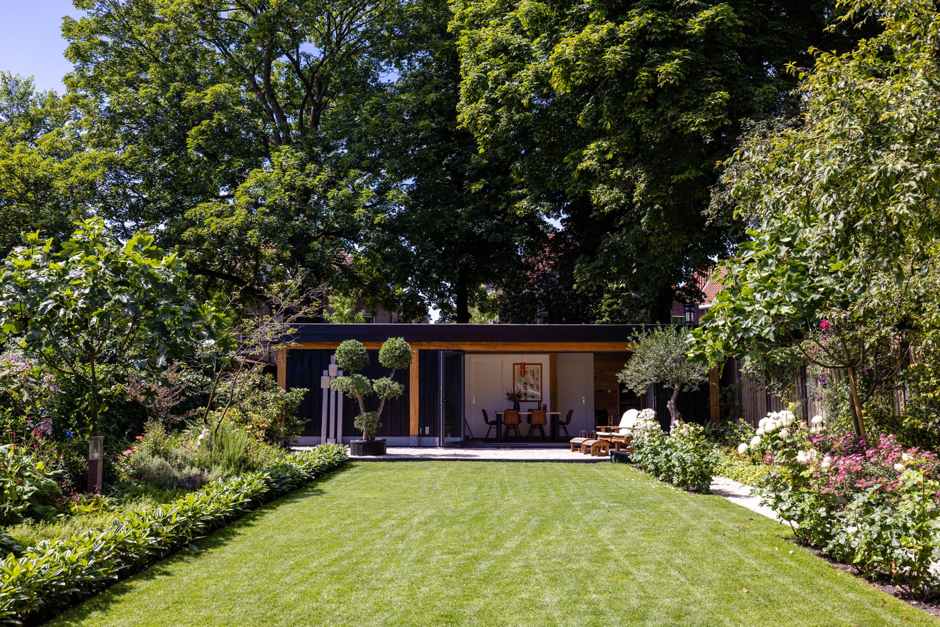 Een grote tuin met een prachtig groen gazon, en mooie plantenborders aan weerszijden van de tuin.